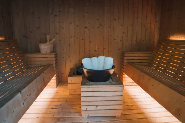 stock image A serene and inviting sauna interior featuring warm wooden paneling, ambient lighting, and a central table with rolled white towels in a black bowl, exuding luxury.