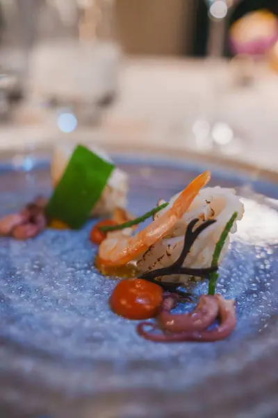 stock image A beautifully plated gourmet seafood dish featuring shrimp and octopus, garnished with green vegetables and orange sauce, set in an elegant luxury hotel restaurant.