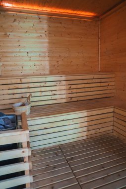 Lüks bir sauna odasında hafif ahşap paneller, banklar ve temel buhar aletlerinin kullanıldığı bir deneyim rahatlama. Ilık aydınlatma sıcak atmosferi güçlendirir.