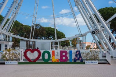 İtalya, Sardinya 'da kalp sembolü ve dönme dolap ile canlı Olbiya işareti. Yeşillik ve açık mavi gökyüzü davetkar ve büyüleyici bir atmosfer yaratır..