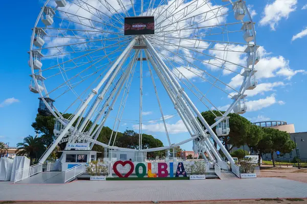 Olbia, Sardinya 'nın cazibesini deneyin. Mavi bir gökyüzüne kurulmuş büyük bir dönme dolap ile. Yeşillik ve hoş geldin işareti canlandırır..