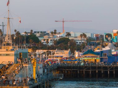 Los Angeles 'taki Santa Monica İskelesi' nde kalabalık bir kalabalık, ikonik dönme dolap, palmiye çizgili sokaklar ve öğleden sonra ışıklarının altında uzak bir vinç bulunuyor..