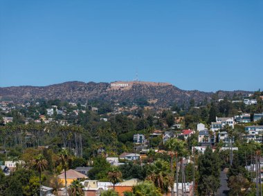 İkonik Hollywood tabelası Los Angeles 'ın yukarısındaki tepelerde, yemyeşil ve açık mavi gökyüzünün altındaki yerleşim yerleriyle çevrili..