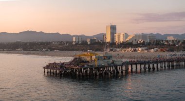 Santa Monica İskelesi Pasifik Okyanusu 'na kadar uzanır, bir dönme dolap ve cazibesi vardır. Şehir manzarası ve dağlar sıcak bir günbatımı parıltısının altında görülebilir..