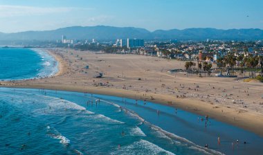 Los Angeles, Kaliforniya 'daki Venice Beach' in hava görüntüleri, kumlu kıyılar, sahile gidenler, şehir binaları ve Santa Monica Dağları.