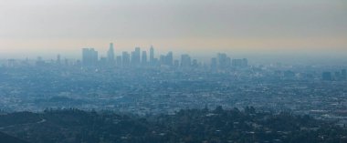 Los Angeles ufuk çizgisi yukarıdan görülür. Uzakta gökdelenler ve ön planda yuvarlanan tepeler açık bir sis bulutuyla kaplanır..