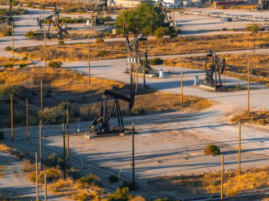Petrol kuleleri Kaliforniya 'da kurak bir çöl arazisine saçılmış, toprak yollar ve sıcak, altın ışıklı altında seyrek bitki örtüsü var..