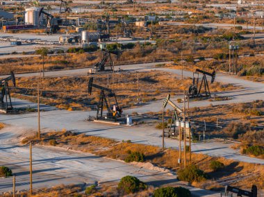Kaliforniya 'da tozlu yolları ve seyrek bitkileri olan bir çöl arazisinde sayısız petrol kulesi faaliyet gösteriyor. Batan güneş sahnenin üzerine uzun gölgeler serer..