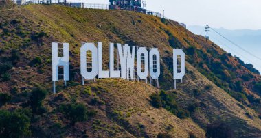 Sembolik Hollywood tabelası dağınık bitki örtüsü olan çimenli bir yamaca asılmış. Büyük beyaz harfler açıyla kısmen gizlenmiş..