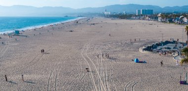 Los Angeles, Kaliforniya 'da Venedik Plajı, Pasifik Okyanusu, kumlu kıyılar, palmiye ağaçları ve Santa Monica Dağları ile bir şehir manzarası içerir..