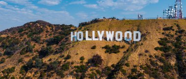 Sembolik Hollywood tabelası Los Angeles 'ta açık mavi gökyüzünün altındaki engebeli tepelerde bulunuyor. İletişim kuleleri görülebiliyor, bu da sahneye modern bir element ekliyor..