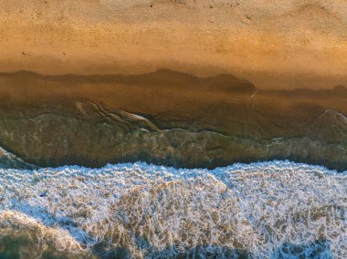 Bir hava perspektifi okyanus dalgalarını yakalar ve pürüzsüz kumlu sahile ulaştıklarında beyaz köpük desenleri oluşturur..