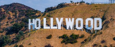 Hollywood tabelası Los Angeles 'ta açık bir gökyüzünün altında kuru arazi ve çalılıklara karşı beyaz harflerle Lees Dağı tepelerinde sergileniyor..