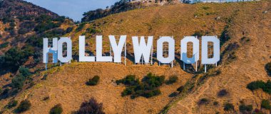 Hollywood tabelası, açık mavi gökyüzünün altında yeşil çalılar ve ağaçlarla çevrili, Lee Dağı 'nın kuru, çimenli tepelerinde belirgin bir şekilde sergilenmektedir..