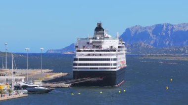 Sardunya limanına büyük bir yolcu gemisi yanaştı. Etrafı engebeli dağlar, sakin sular ve açık mavi gökyüzünün altında daha küçük yatlarla çevrili..