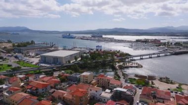 Modern binalar ve berrak mavi suyla çevrili Olbias marinasına bir yelkenli yanaşıyor ve doğal güzelliğin ve şehir hayatının karışımını sergiliyor..
