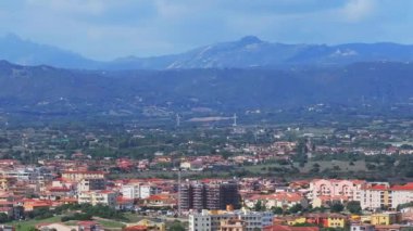 Olbia, Sardinya 'da hareketli bir meydanda bir atlıkarınca, terasotta çatısı olan binalar, açık kafeler, dükkanlar ve palmiye ağaçları yer alıyor ve canlı bir atmosferi yakalıyor..