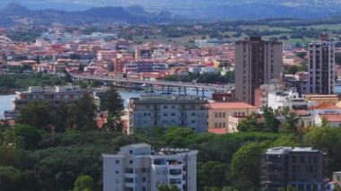 Olbia, Sardinya 'da hareketli bir meydanda bir atlıkarınca, terasotta çatısı olan binalar, açık kafeler, dükkanlar ve palmiye ağaçları yer alıyor ve canlı bir atmosferi yakalıyor..