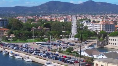 Modern binalar ve berrak mavi suyla çevrili Olbias marinasına bir yelkenli yanaşıyor ve doğal güzelliğin ve şehir hayatının karışımını sergiliyor..
