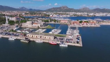 Modern binalar ve berrak mavi suyla çevrili Olbias marinasına bir yelkenli yanaşıyor ve doğal güzelliğin ve şehir hayatının karışımını sergiliyor..