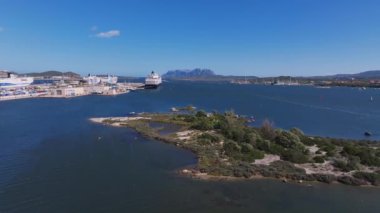 Modern binalar ve berrak mavi suyla çevrili Olbias marinasına bir yelkenli yanaşıyor ve doğal güzelliğin ve şehir hayatının karışımını sergiliyor..