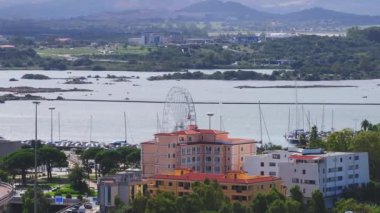 Modern binalar ve berrak mavi suyla çevrili Olbias marinasına bir yelkenli yanaşıyor ve doğal güzelliğin ve şehir hayatının karışımını sergiliyor..