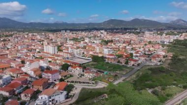 Olbia, Sardinya 'da hareketli bir meydanda bir atlıkarınca, terasotta çatısı olan binalar, açık kafeler, dükkanlar ve palmiye ağaçları yer alıyor ve canlı bir atmosferi yakalıyor..