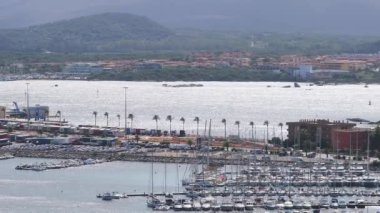 Modern binalar ve berrak mavi suyla çevrili Olbias marinasına bir yelkenli yanaşıyor ve doğal güzelliğin ve şehir hayatının karışımını sergiliyor..