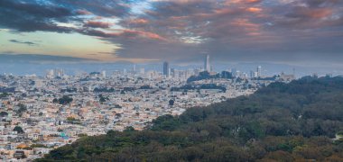 San Franciscos ufuk çizgisinin havadan görünüşü. Satış Gücü Kulesi ve Transamerica Piramidi. Yoğun şehir manzarası, bulutlu bir gökyüzü altında yeşillik..