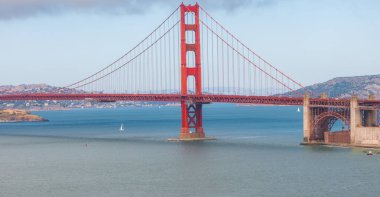 San Francisco, Kaliforniya 'daki Golden Gate Köprüsü, Uluslararası Turuncu' da mavi sulara ve uzak tepelere karşı, körfezde yelkenli tekneleriyle ayakta duruyor..