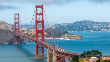 Golden Gate Köprüsü San Francisco Körfezi 'nin mavi sularını kaplar. Uluslararası Turuncu rengi, yuvarlanan tepeler ve bulutlu gökyüzü ile çelişir..