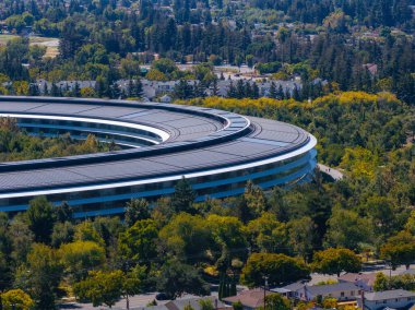 Görüntü, Cupertino, California 'da yeşillikler, yerleşim yerleri ve ormanlarla çevrili dairesel Apple Park kampüsünü yakalıyor..