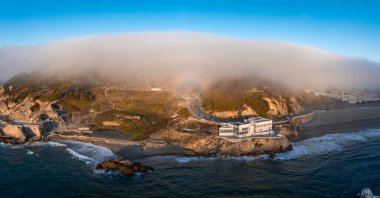 Pasifik Okyanusu 'nun üzerindeki ikonik Cliff House' un altında dalgalar çarpıyor ve San Francisco, Kaliforniya 'daki tepeleri sis kaplıyor..