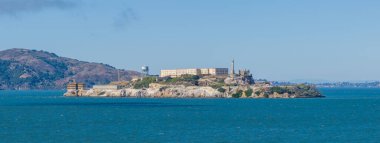 Alcatraz Adası 'nın arka planında San Francisco Rıhtımı mavi suları ve Marin Burnu ile çevrili tarihi cezaevi ve gözlem kulesi yer almaktadır..