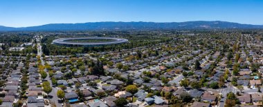 The image shows Apple Parks circular building amidst greenery and homes, with the Santa Cruz Mountains in the background, in Cupertino, California. clipart