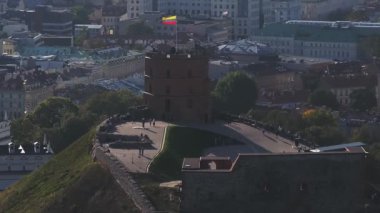 Gediminas Kulesi Litvanya bayrağının yanında duruyor. Etrafı yemyeşil ve Litvanya 'nın Vilnius kentindeki tarihi kilise kuleleri ile çevrili..