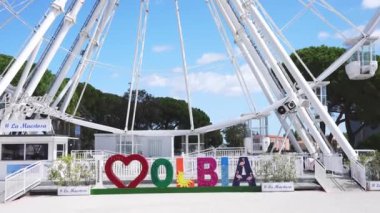 Olbia, Sardinya, İtalya 'da büyük bir dönme dolap. Etrafı palmiye ağaçları ve açık mavi gökyüzü ile çevrili. Güneşli bir günde insanlar etrafta geziniyor..