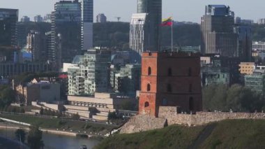 Gediminas Kulesi Litvanya bayrağının yanında duruyor. Etrafı yemyeşil ve Litvanya 'nın Vilnius kentindeki tarihi kilise kuleleri ile çevrili..
