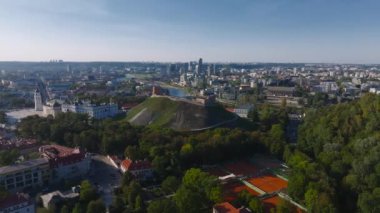 Gediminas Kulesi Litvanya bayrağının yanında duruyor. Etrafı yemyeşil ve Litvanya 'nın Vilnius kentindeki tarihi kilise kuleleri ile çevrili..