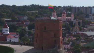 Gediminas Kulesi Litvanya bayrağının yanında duruyor. Etrafı yemyeşil ve Litvanya 'nın Vilnius kentindeki tarihi kilise kuleleri ile çevrili..