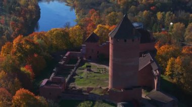 Sigulda, Letonya 'nın hava manzarası, açık mavi gökyüzü altında canlı sonbahar yaprakları ve Turaida Kalesi, mevsimsel güzellikleri vurguluyor..