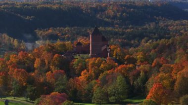 Sigulda, Letonya 'nın hava manzarası, açık mavi gökyüzü altında canlı sonbahar yaprakları ve Turaida Kalesi, mevsimsel güzellikleri vurguluyor..