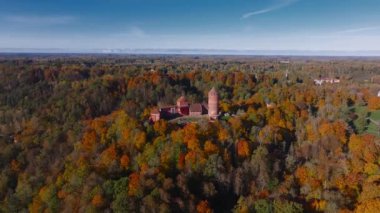 Sigulda, Letonya 'nın hava manzarası, açık mavi gökyüzü altında canlı sonbahar yaprakları ve Turaida Kalesi, mevsimsel güzellikleri vurguluyor..