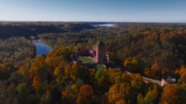 Sigulda, Letonya 'nın hava manzarası, açık mavi gökyüzü altında canlı sonbahar yaprakları ve Turaida Kalesi, mevsimsel güzellikleri vurguluyor..