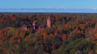 Sigulda, Letonya 'nın hava manzarası, açık mavi gökyüzü altında canlı sonbahar yaprakları ve Turaida Kalesi, mevsimsel güzellikleri vurguluyor..