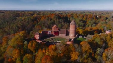 Sigulda, Letonya 'nın hava manzarası, açık mavi gökyüzü altında canlı sonbahar yaprakları ve Turaida Kalesi, mevsimsel güzellikleri vurguluyor..