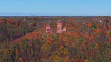 Sigulda, Letonya 'nın hava manzarası, açık mavi gökyüzü altında canlı sonbahar yaprakları ve Turaida Kalesi, mevsimsel güzellikleri vurguluyor..