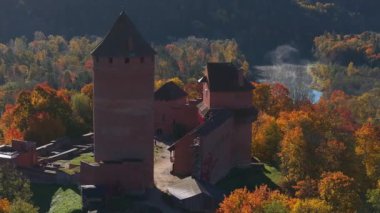 Sigulda, Letonya 'nın hava manzarası, açık mavi gökyüzü altında canlı sonbahar yaprakları ve Turaida Kalesi, mevsimsel güzellikleri vurguluyor..