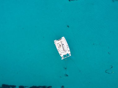 Beyaz bir katamaran Sardunya kıyılarının açık, turkuaz sularına demirlemiş. Titreşimli deniz, dingin okyanusla çelişen koyu beneklere sahiptir..