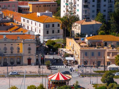 Olbias merkez plazasında, terasotta çatıları ve hareketli kalabalıklarla çevrili renkli bir atlıkarınca yer almaktadır..